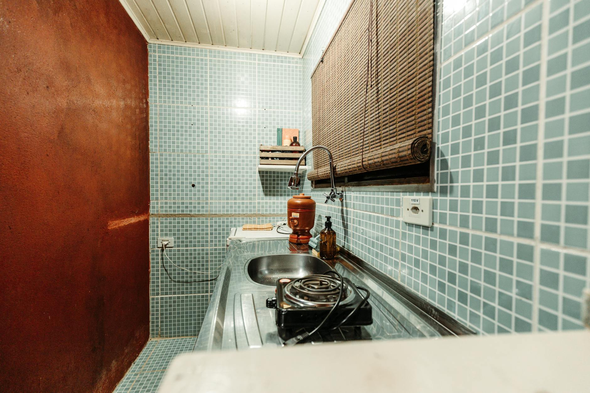 Mały aneks kuchenny z niebieskimi płytkami, zlewem i jednopalnikową kuchenką