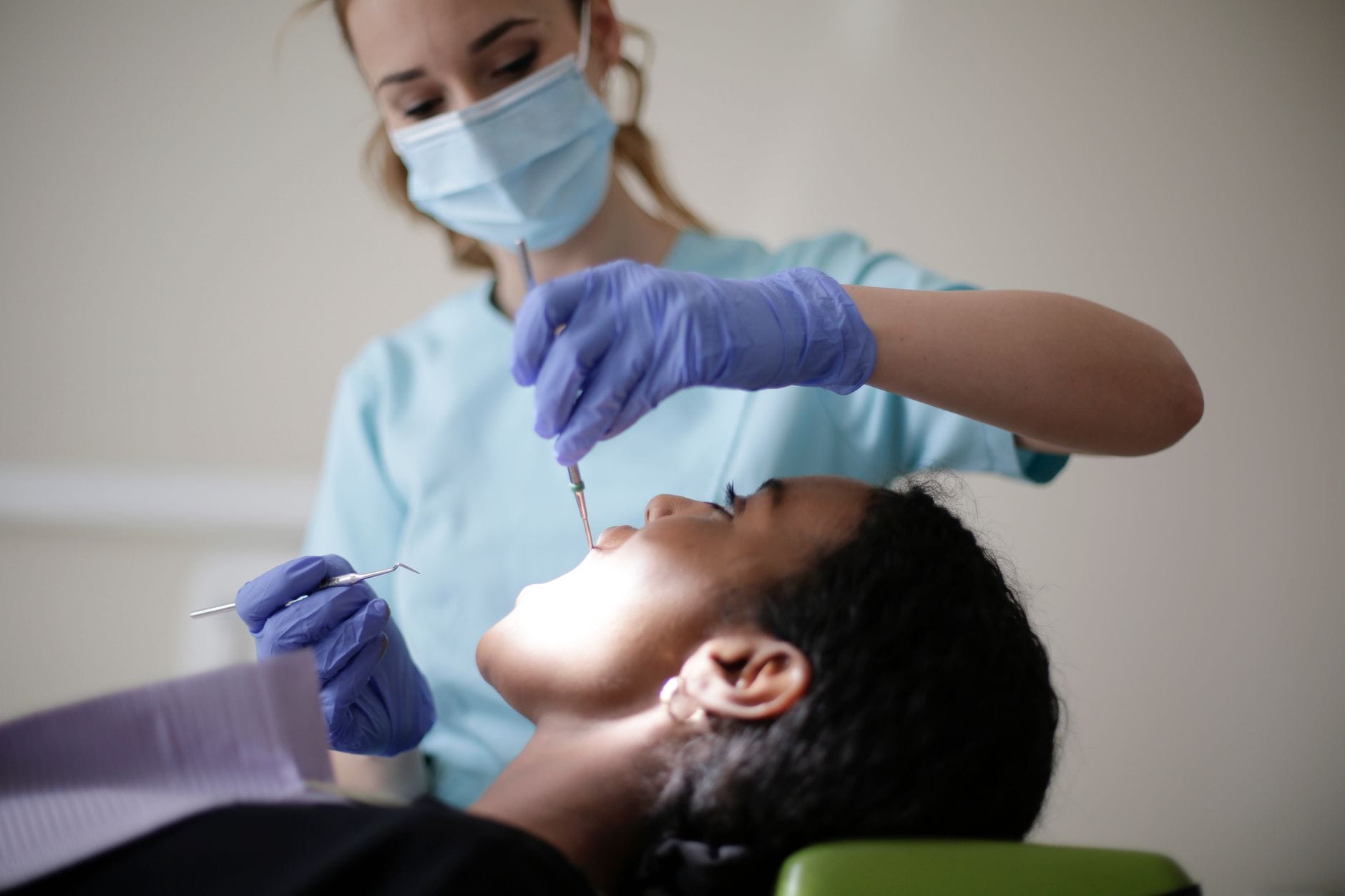 Dentysta w maseczce bada zęby dorosłego czarnoskórego pacjenta w gabinecie