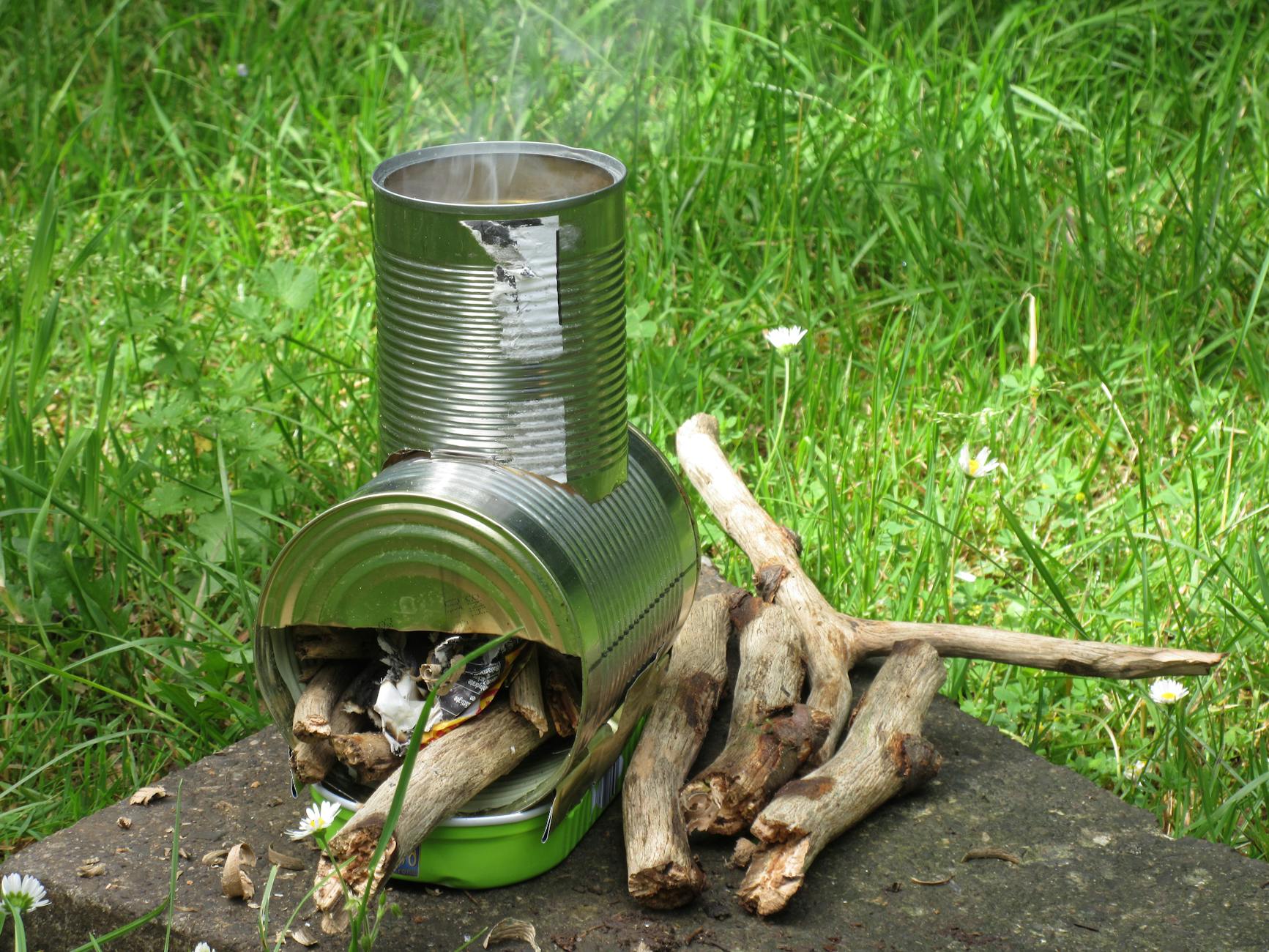 Piec z puszki na gałęzie na trawie podczas biwaku bushcraftowego